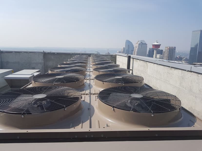 Commercial rooftop HVAC condenser installation with Calgary Tower skyline — multiple cooling units arranged in parallel rows