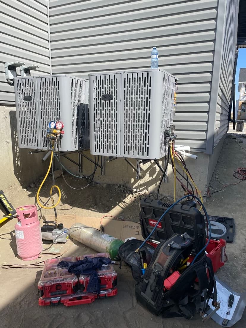 HVAC technician manifold gauges and vacuum pump setup during refrigerant line commissioning on dual condenser installation