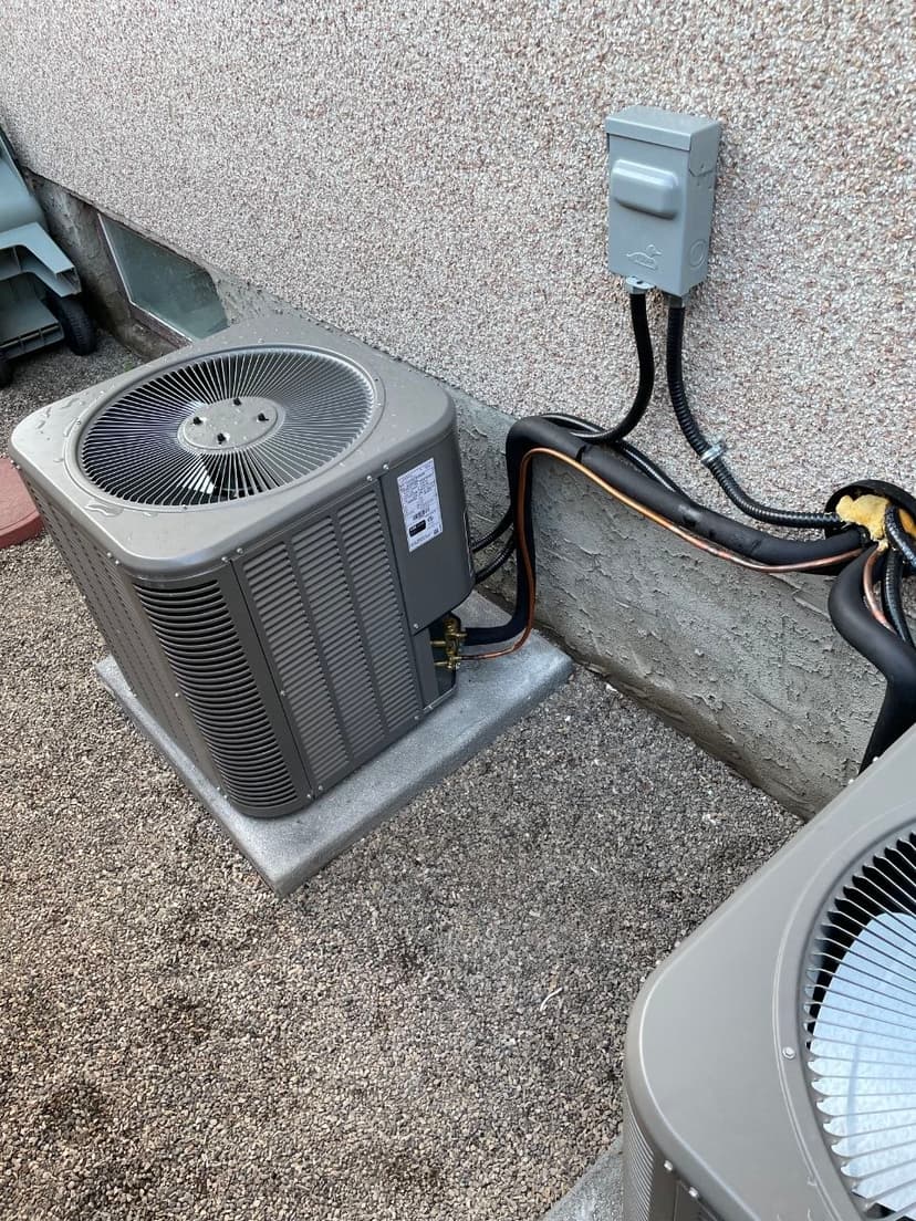 Outdoor HVAC condenser with electrical disconnect box, liquid-tight conduit, and copper lines against stucco wall