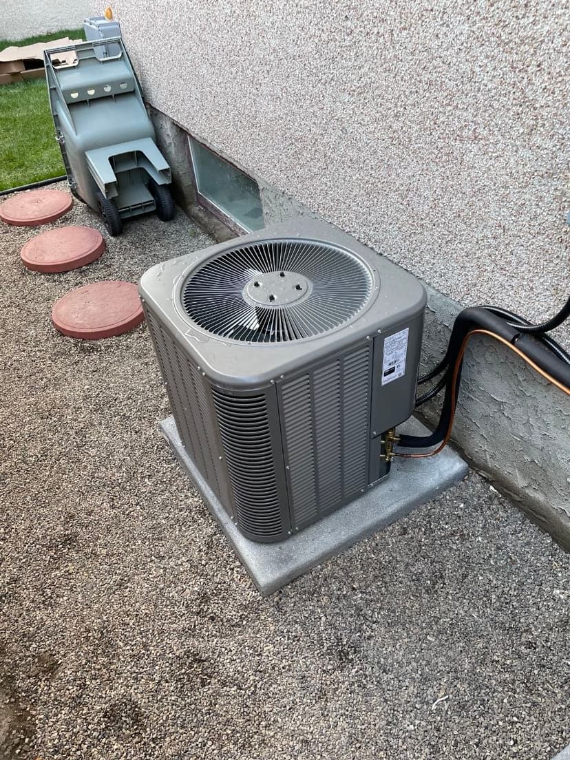 Residential outdoor air conditioning condenser unit on concrete pad with copper refrigerant lines and electrical conduit